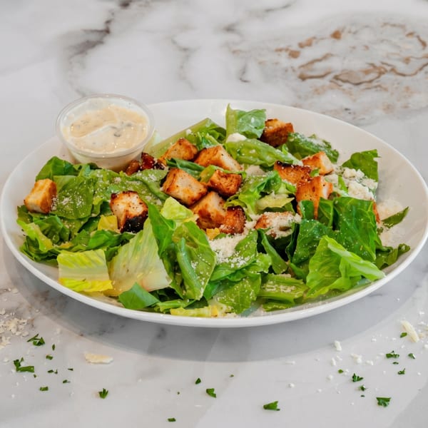 Fresh Caesar salad with crisp romaine, croutons, parmesan, and creamy dressing on a white plate.