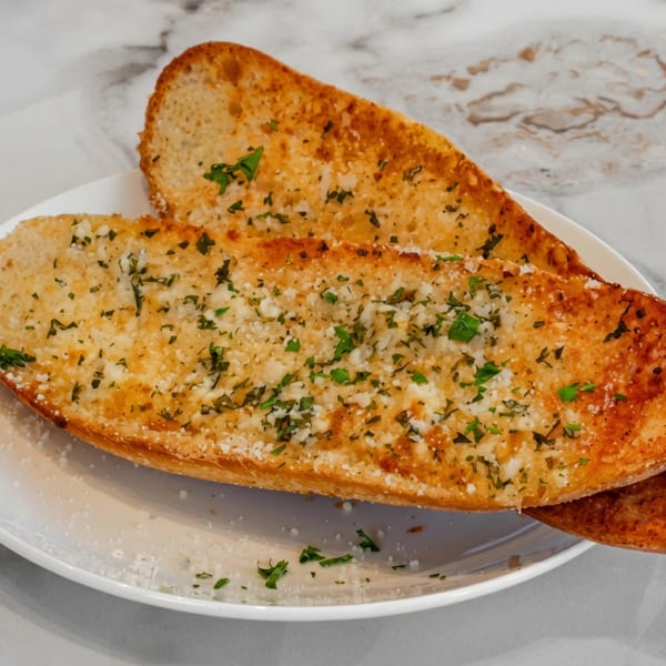 Two slices of golden-brown garlic bread with parsley and parmesan cheese on a white plate.