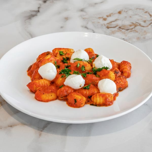 Gnocchi with red sauce, fresh mozzarella balls, and parsley on a white plate.
