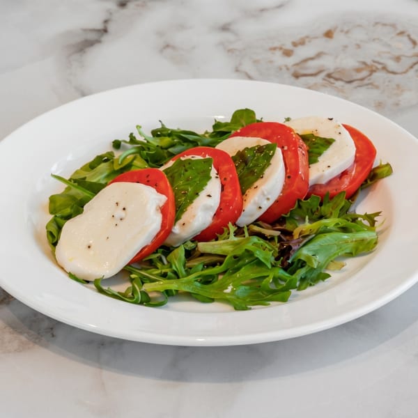 Caprese salad with sliced tomatoes, mozzarella, basil, and arugula on a white plate.